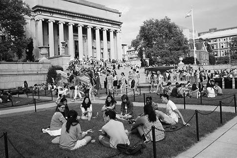 Roughly a dozen students sit in a circle on a grassy patch near the steps of Low Memorial Library on a bright, sunny day