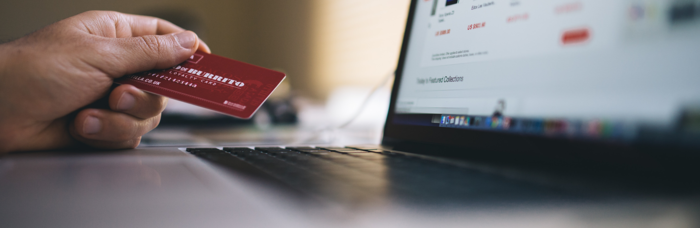 A hand holding a credit card next to a laptop